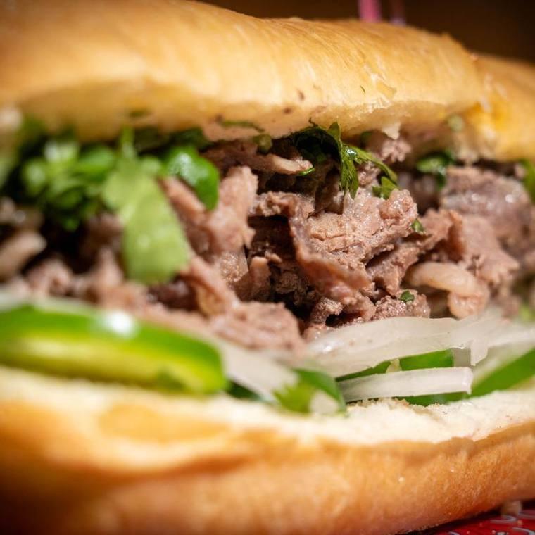 Banh mi cut open showing sliced beef, cilantro, jalapeno, and pickled vegetables