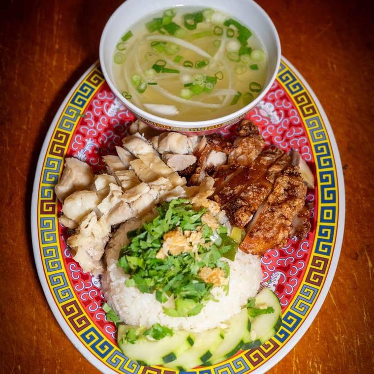 Chicken rice plate with poached and fried chicken, cucumber, herbs, and a bowl of clear broth